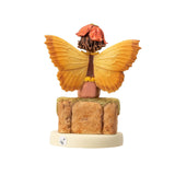 Fairy figurine of a boy with brown and yellow top, tan pants, sitting on a wall with a flower hat. Base says "Wallflower Fairy"