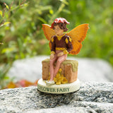 Fairy figurine of a boy with brown and yellow top, tan pants, sitting on a wall with a flower hat. Base says "Wallflower Fairy"