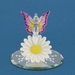 Figurine by Glass Baron. A clear glass fairy with pink and yellow wings sits on a white daisy flower with a yellow center. The pixie has yellow crystal accents on the wings. The base of the piece is a mirror with white designs. 