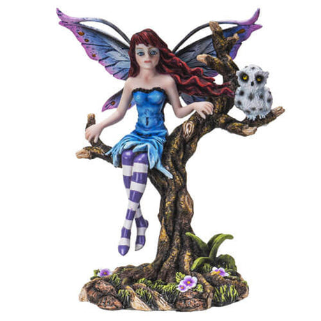 The fairy perches on a tree. On the branch next to her, is a white owl with black spots. The fae has a blue dress, purple and white striped stockings, and indigo wings to match! Her red hair flutters in the breeze, and flowers bloom below. 