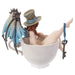 Fairy with steampunk wings in blue and a tophat, and a key looped around her leg. She sits in a teacup, taking a bath. Shown from the back. She has red hair.