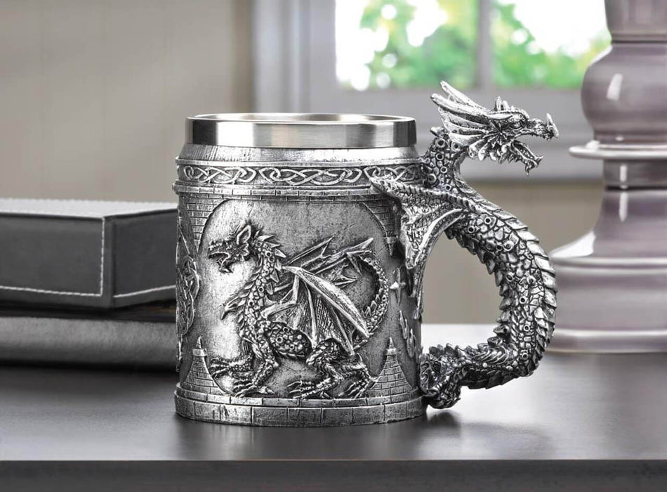Silver-toned mug with scene of a dragon, and dragon handle. Stainless steel insert. Shown on a table