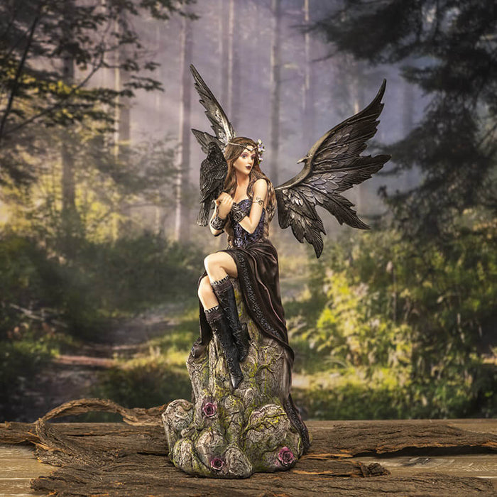 Crow and fairy figurine shown in a forest setting on a wood table