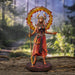 Fire Sorceress figurinec clad in red, orange and black clothes, holding a staff with a ring of fire around her horned head. Stands on black decorated base. Shown on a forest background