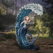 Water sorceress mermaid with blue scales and two fish, with a wave of water curling up around her. Shown against a forest backdrop