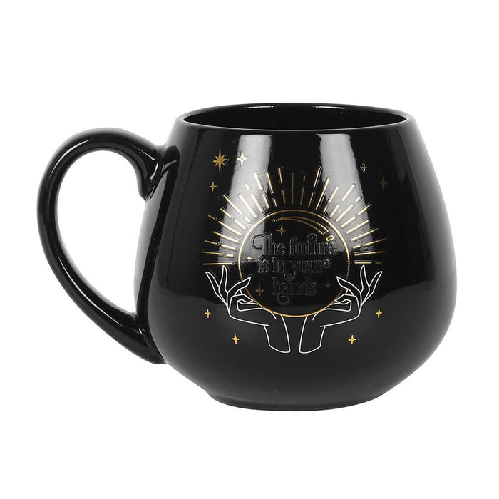 Fortune Teller Color Change mug. Black base with hands and a crystal ball. The words "The future is in your hands" are revealed when a hot beverage is poured in