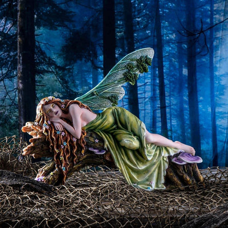 The statue features a lovely pixie sleeping on a forest log. The fae lady has a green dress and leafy emerald dragonfly wings to match. Her red-brown hair is adorned with colorful flower blossoms, and purple mushrooms sprout from the wood she slumbers on. Image shows the piece set with a dark forest background