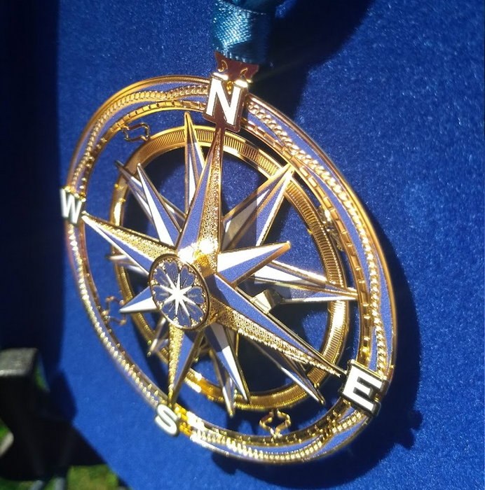 Compass ornament shown in the sun on a blue backdrop