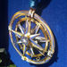 Compass ornament shown in the sun on a blue backdrop