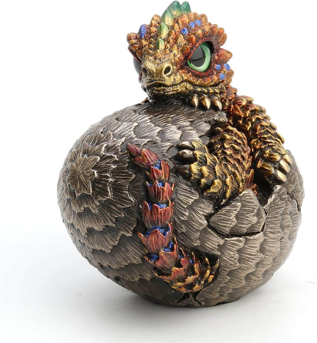 Baby dragon hatching from egg, done in shades of gold and red with blue and yellow accents and a green eye. Shown from the front