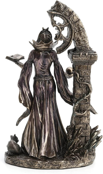 Back view - Aradia s represented standing with eyes closed, face tipped to the heavens. Her dress is long and flowy, and she holds a tome in one hand and an orb in the other. She stands in front of ruins twined with vining flowers. 