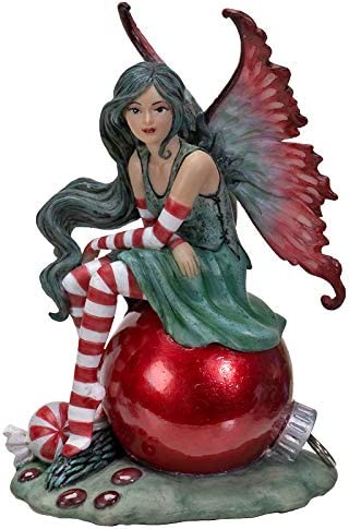 Fairy sitting on a red Christmas ornament. She wears a green dress with red & white striped stockings and sleeves and there is a peppermint nearby.