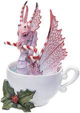 Pink and red dragon sitting in a cup, holding a candy cane in its mouth. Holly leaves and berries sit at the base of the cup. Side view