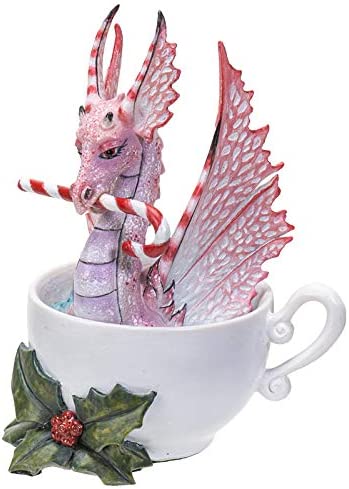 Pink and red dragon sitting in a cup, holding a candy cane in its mouth. Holly leaves and berries sit at the base of the cup. Side view