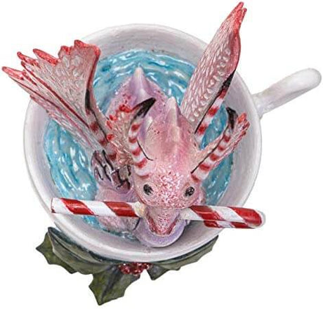 Top down view Pink and red dragon sitting in a cup, holding a candy cane in its mouth. Holly leaves and berries sit at the base of the cup.