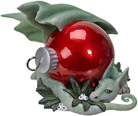 Green dragon figurine with red Christmas ornament and white berries.