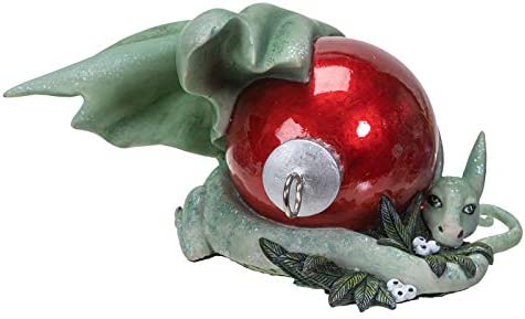 Green dragon figurine with red Christmas ornament and white berries. Shown from the side, to see dragon's face