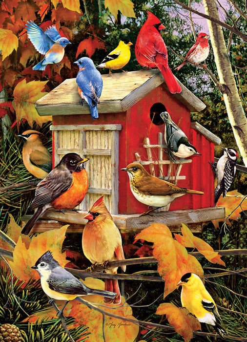 A flock of all different bird species gather round a charming red barn birdhouse. Autumn leaves show the season.