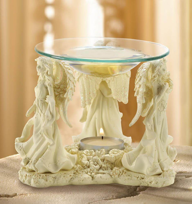 Trio of angels with glittering wings hold up a glass bowl to melt a scented wax cube or oil. A place underneath, decorated with flowers, holds a tea light candle.