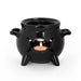 Glossy black cauldron mug warmer shown on its own with a lit tealight inside, seen through a triple moon cutout