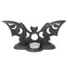 Black bat tealight holder with wings outstretched, and moon phases cut out to show the candlelight. Shown with unlit candle from the back