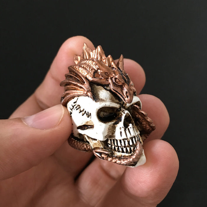 Miniature figurine of a bronze dragon curling around and through a human skull. Shown held in a hand, it is small
