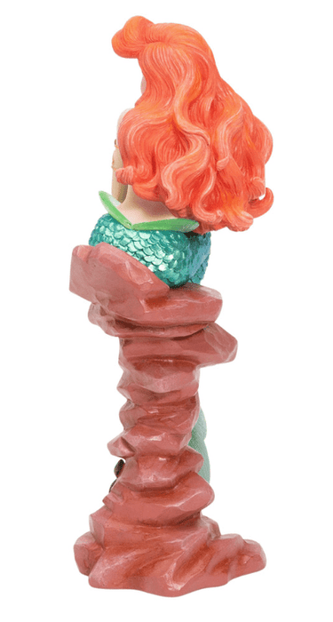 Disney's Ariel, the Little Mermaid, sits and ponders. She has a shiny metallic tail and bright red hair. Back view of rock and hair