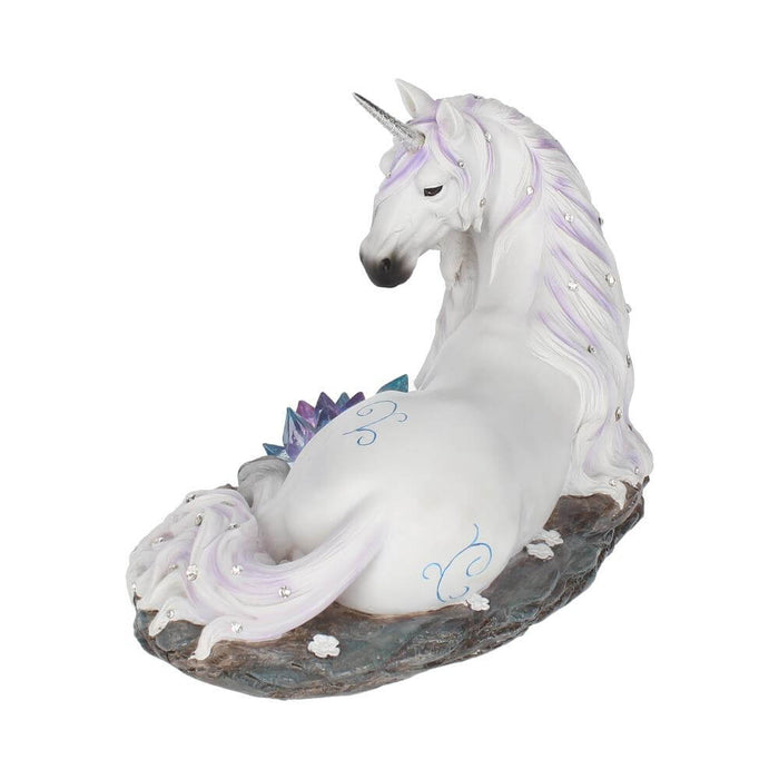 White unicorn with jewels in mane and tail laying down near blue-purple crystals. View showing hindquarters with blue swirl designs