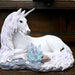 White unicorn with jewels in mane and tail laying down near blue-purple crystals