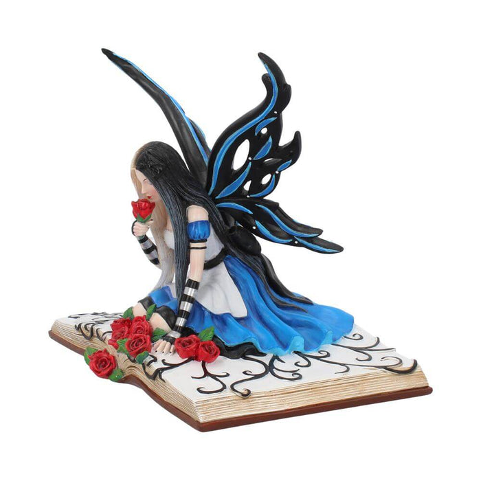 Alice in Wonderland inspired fairy with blue and black wings, a blue and white dress, and split hair colors. She sits on a storybook covered in red roses and black swirls. Side view showing black part of hair