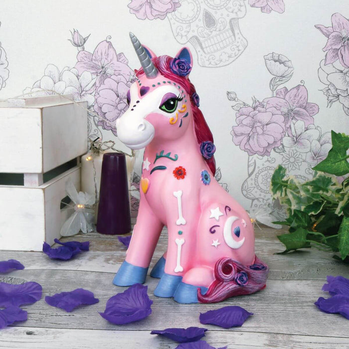 Pink unicorn with sugar skull theme sitting amidst purple flower petals