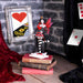 Queen of Hearts figurine - fairy with red and black dress, white and black stockings, red, purple and black wings standing on playing cards. Displayed on a stack of small leather books with playing cards in the background