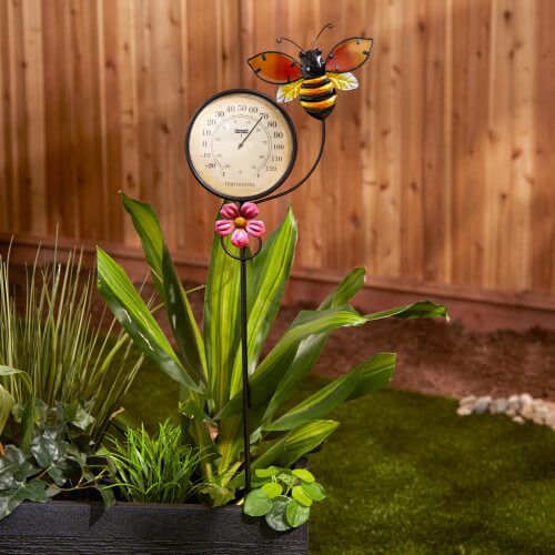Garden stake with bee, thermometer and pink flower shown in a yard setting
