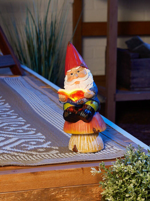 Gnome sitting on mushroom reading a book Shown at night with the book glowing via solar light, sitting on the edge of a deck rug