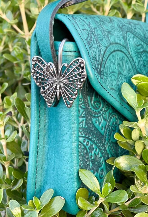 Butterfly purse hook shown on a teal purse amidst leaves