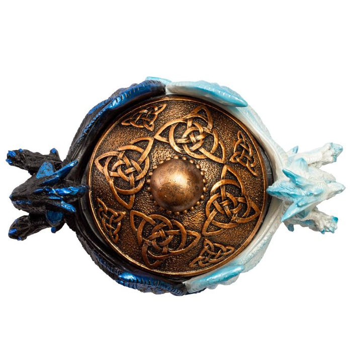 View of trinket box from above. Black dragon and white dragon, both accented in blue, wings curved around a gold box with Celtic knot designs on the lid