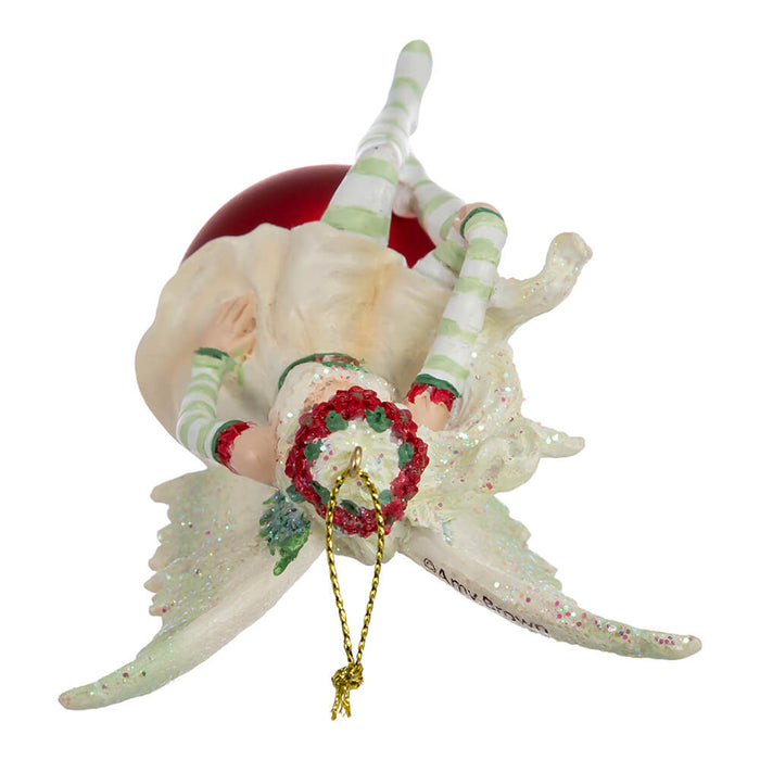Top down view of Amy Brown fairy ornament in shades of green and white, with pixie sitting on a red ornament ball.