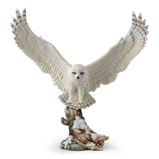 White snowy owl with wings spread to either side, in flight. Below is a snow covered tree branch