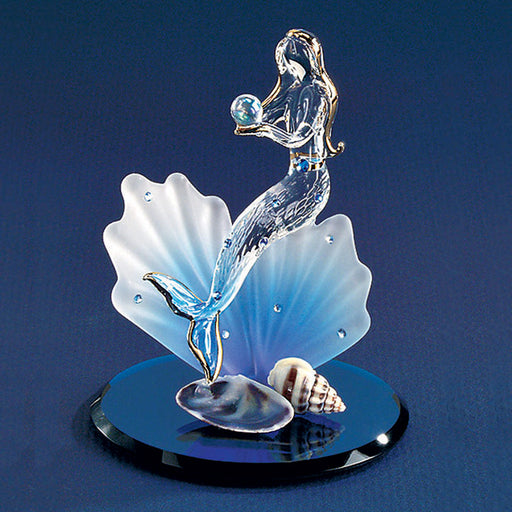 Glass figurine of a clear mermaid with golden accents on hair and fins, holding a pearl. She sits upon a blue and white frosted glass seashell studded with Austrian crystals. The base of the piece is mirrored with two seashells.