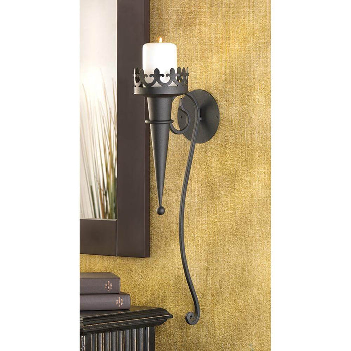 Torch Gothic Candle Sconce hung on a tan wall with a lit pillar candle