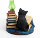 Black cat reading a book next to more tomes and a green lamp. Shown from the back