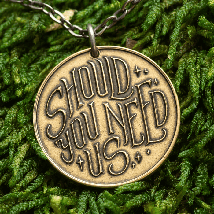 Back of coin pendant with text "Should You Need Us"