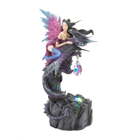 Figurine showing a dragon with pink and blue wings in a purple dress and indigo stockings. She holds onto a purple dragon who has a crystal dangling from its claws. The figurine lights up with a small LED