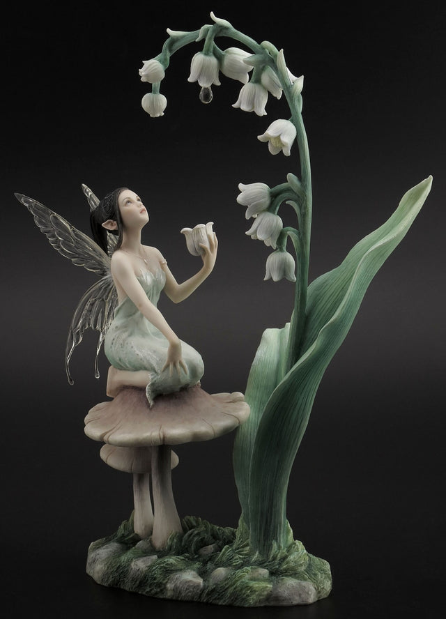 Lily of the Valley figurine showing a fairy with transparent wings on a mushroom, holding a flower and looking up at more lily of the valley blooms