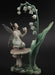 Lily of the Valley figurine showing a fairy with transparent wings on a mushroom, holding a flower and looking up at more lily of the valley blooms