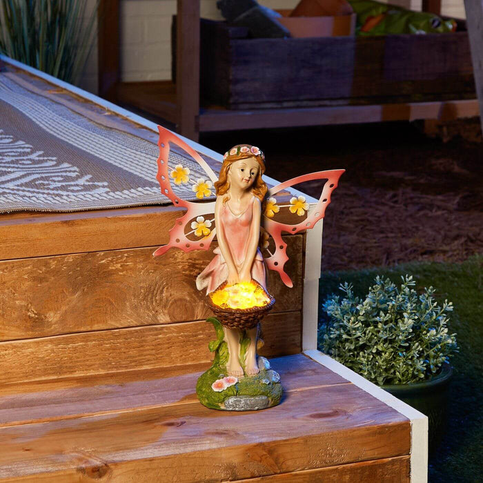 Fairy in a pink dress with basket of flowers that lights up at night. Pink wings with flower accents. Shown at night, glowing, on a wooden garden step