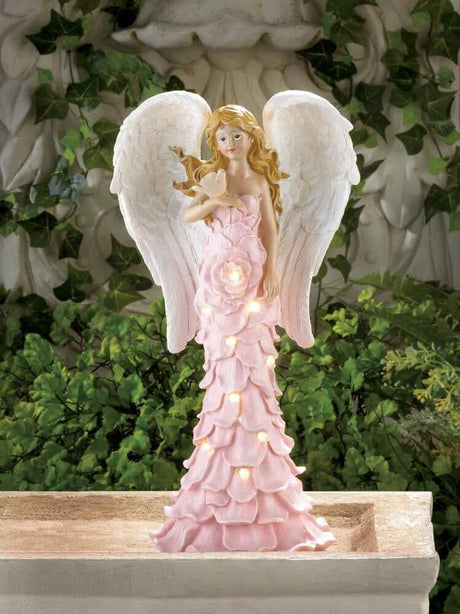 Angel figurine with dove on her hand. Wears a dress of pink rose petals. Shown lit up via solar power and displayed in a garden setting