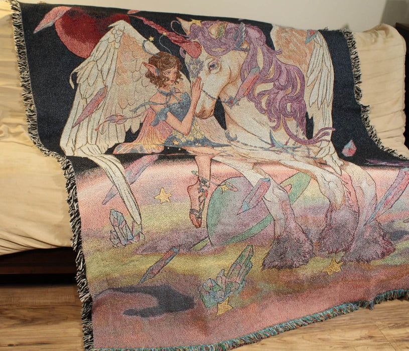 Cosmic fairy and winged unicorn tapestry blanket shown draped over a couch