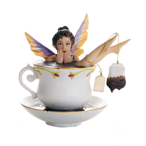 A fairy sits in a teacup, taking a bath. She has a surprised expression and her legs stick out the cup, a teabag wrapped around one