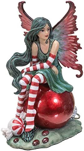 Fairy sitting on a red Christmas ornament. She wears a green dress with red & white striped stockings and sleeves and there is a peppermint nearby. Front view
